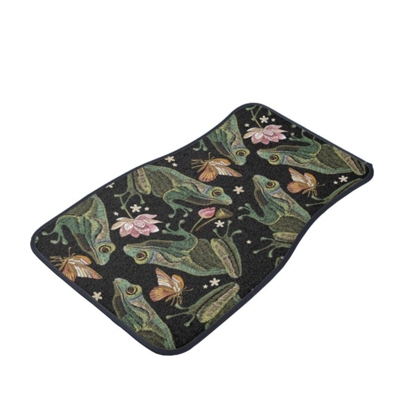 Puede incluir: Una alfombra de ba&ntilde;o negra con un patr&oacute;n repetido de ranas verdes, flores rosas y mariposas. La alfombra tiene un borde azul oscuro.