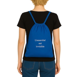 Könnte beinhalten: Ein königsblauer Kordelzugrucksack mit dem französischen Text "L'essentiel est invisible" in Weiß aufgedruckt. Die Tasche ist aus weichem Stoff und hat blaue Kordelzüge.