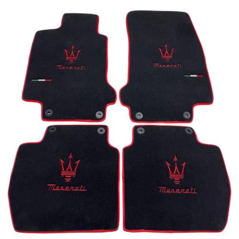 May include: Set of four black car floor mats with red trim. Each mat features a red Maserati logo and the brand name embroidered in red. Includes the Italian flag colors.