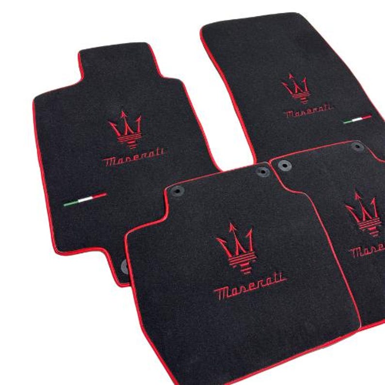 May include: Set of four black car floor mats with red trim. Each mat features the Maserati logo embroidered in red. The mats have an Italian flag detail and are designed to protect the vehicle's interior.