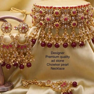 Könnte beinhalten: Ein goldfarbenes Schmuckset mit einer Halskette, Ohrringen und einem Armband. Das Set ist mit roten Edelsteinen und kleinen weißen Perlen verziert. Das Bild enthält den Text: Designer, Premium quality, ad stone, Chowker pearl, Necklace.