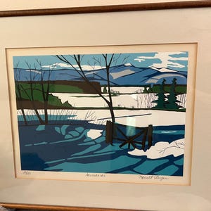 以下が含まれることがあります： 青い山々、緑の木々、白い雪が描かれた冬の風景の額入りプリント。手前には暗い木製の柵と葉のない木々が配置されている。アーティストの署名があり、Adirondacksというタイトルが記されている。