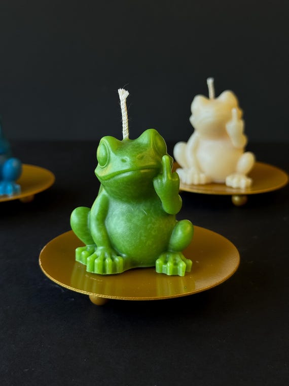 A tiny sculpted frog flipping the bird — functional soy wax candle meets chaotic little art piece you'd actually display.
