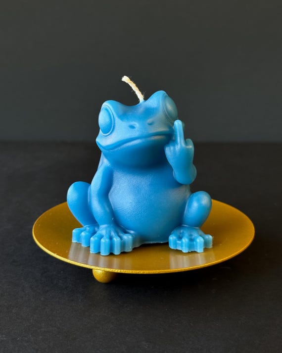 A tiny sculpted frog flipping the bird — functional soy wax candle meets chaotic little art piece you'd actually display.