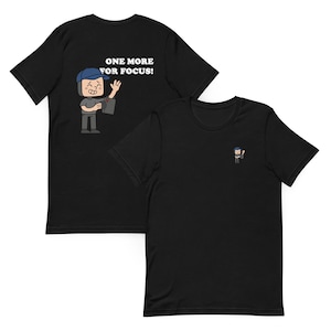 Könnte beinhalten: Schwarze T-Shirts mit einer Cartoon-Grafik. Ein Shirt hat ein Design auf der Rückseite mit dem Text "ONE MORE FOR FOCUS!". Das andere Shirt hat eine kleine passende Grafik auf der Vorderseite. Die Grafik zeigt eine Person, die eine Kamera hält.