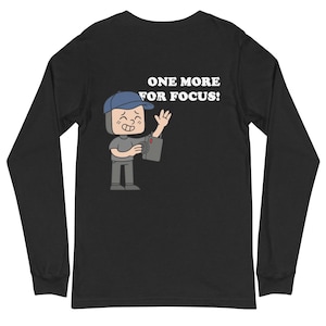 May include: Black long-sleeve shirt with a cartoon illustration of a person holding a camera. The person is wearing a blue cap and gray clothing. The text "ONE MORE FOR FOCUS!" is printed in white.