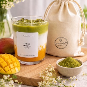 Peut inclure: Une bougie en couches dans un pot en verre avec des sections vertes, blanches et orange, étiquetée "MANGO MATCHA LATTE". Un petit bol beige de poudre verte et un sac en tissu beige sont à côté de la bougie. Une mangue et des fleurs sont également dans l'image.