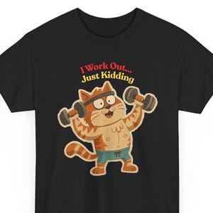Może przedstawiać: Czarny t-shirt z kreskówkowym kotem podnoszącym hantle. Kot jest pomarańczowo-biały, nosi opaskę na głowę i niebieskie szorty. Tekst nad kotem brzmi "I Work Out... Just Kidding" w kolorze czerwonym i czarnym.