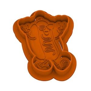 Puede incluir: Un cortador de galletas naranja con forma de personaje de hot dog de dibujos animados que lleva gafas de sol y hace gestos con las manos de rock and roll. El diseño presenta líneas en relieve para imprimir detalles, incluida una línea ondulada.