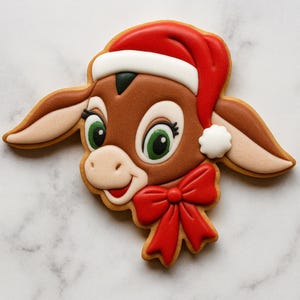 Peut inclure: Un biscuit décoré en forme de tête d'âne de dessin animé portant un bonnet de Père Noël rouge et blanc. L'âne a un pelage marron, de grands yeux verts avec des cils noirs et un nœud rouge vif attaché au cou. Le glaçage est lisse et éclatant.