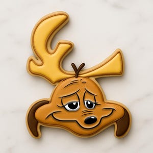 Puede incluir: Una galleta decorada con forma de cabeza de personaje de dibujos animados con grandes cuernos. La galleta presenta tonos marrones y amarillos con detalles en blanco y negro, y una expresión triste.