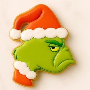 May include: A green cookie shaped like a character's face, wearing a red Santa hat with white trim. The cookie has a grumpy expression with a yellow eye and is decorated with icing.