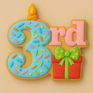 Puede incluir: Una galleta decorada con la forma del número 3 con las letras "rd" en rosa. El número 3 es azul con chispas de colores y una vela. También se incluye una caja de regalo roja con un lazo verde.