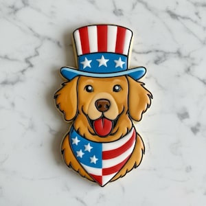 May include: A dog-shaped biscuit decorated with icing in patriotic colours. The golden retriever wears a blue hat with white stars and a red, white, and blue bandana. The biscuit has a smiling face and a red tongue.
