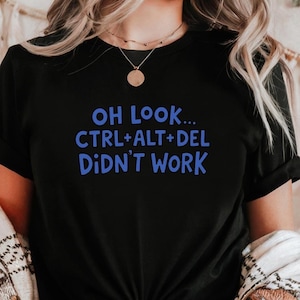 Puede incluir: Camiseta negra con el texto azul "OH LOOK... CTRL+ALT+DEL DIDN'T WORK". La camiseta es de cuello redondo y parece estar hecha de un material suave. El texto está centrado en la parte delantera de la camiseta.