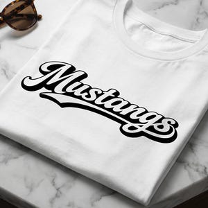 May include: White t-shirt with the word "Mustangs" in a black and white script design. The shirt is folded neatly on a marble surface, with sunglasses and a watch nearby.