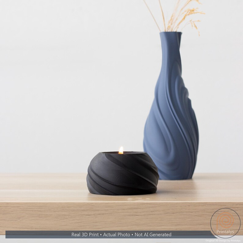 May include: A black, spiral-textured candle holder with a lit candle is on a wooden surface. A blue vase with a similar spiral design and dried plants is in the background. The text at the bottom reads: Real 3D Print &bull; Actual Photo &bull; Not AI Generated.
