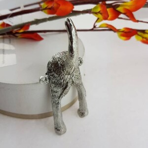May include: Silver metal dog tail hook. The hook is shaped like a dog's rear end with its tail sticking straight up in the air.