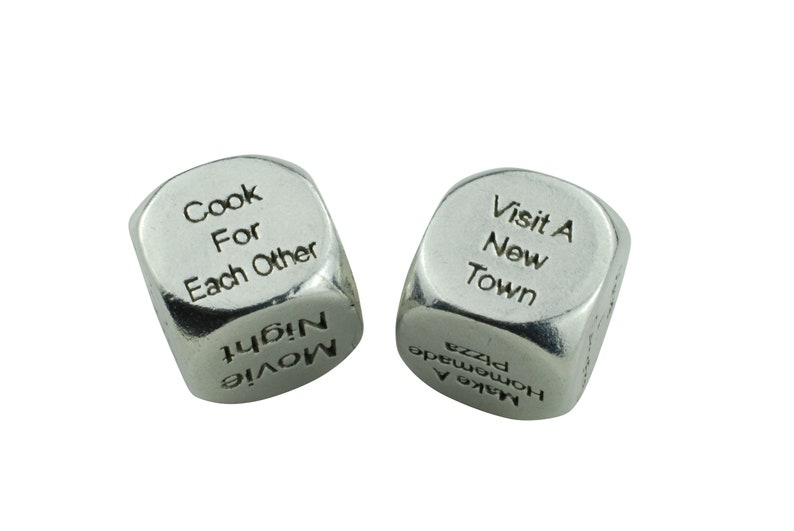 May include: Two silver dice with different phrases on each side. The first die has the phrases "Cook For Each Other" and "Movie Night". The second die has the phrases "Visit A New Town" and "Make A Homemade Pizza".
