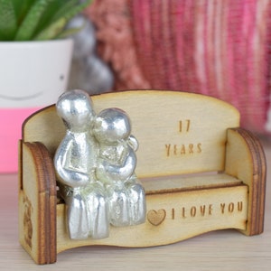 May include: A wooden bench with two silver figurines of a couple sitting on it. The bench has the text "17 Years" and "I Love You" engraved on it.