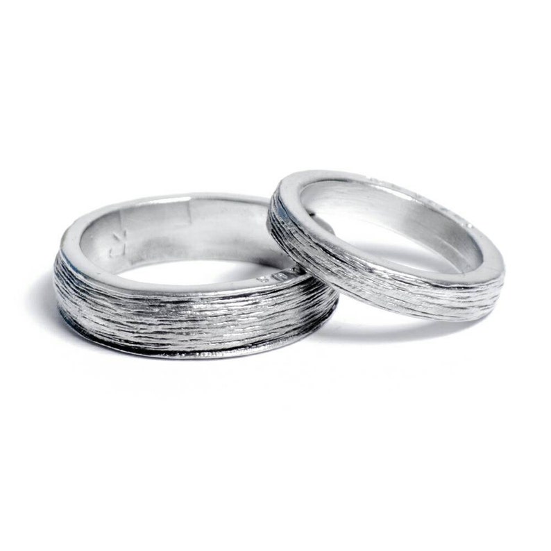 May include: Two silver wedding bands with a textured, brushed finish.