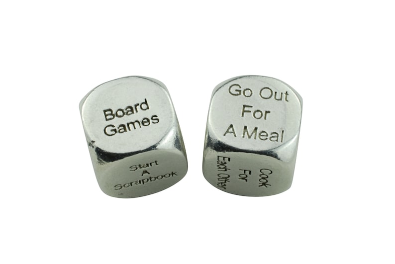 May include: Two silver dice with different activities printed on each side. The first die has "Board Games" and "Start A Scrapbook" printed on it. The second die has "Go Out For A Meal" and "Cook For Each Other" printed on it.