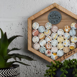 May include: A hexagonal wooden frame with a glass front holds a collection of colorful round ceramic tiles. Each tile features a different design, including flowers, waves, and abstract patterns. The frame is labeled "Our Dates" and "5 years".