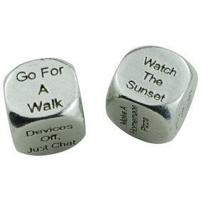 May include: Two silver dice with different phrases on each side. The first die has the phrases "Go For A Walk", "Devices Off, Just Chat", "Make A Wish", "Take A Nap", "Read A Book", and "Have A Drink". The second die has the phrases "Watch The Sunset", "Make A Homemade Pizza", "Go To The Beach", "Have A Picnic", "Go For A Run", and "Play A Game".