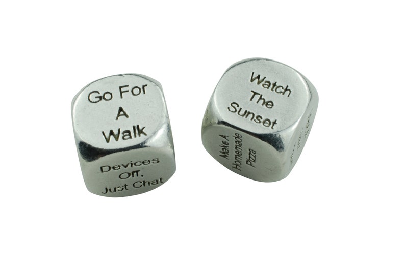 May include: Two silver dice with different phrases on each side. The first die has the phrases "Go For A Walk", "Devices Off, Just Chat", "Make A Wish", "Take A Nap", "Read A Book", and "Have A Drink". The second die has the phrases "Watch The Sunset", "Make A Homemade Pizza", "Go To The Beach", "Have A Picnic", "Go For A Run", and "Play A Game".
