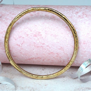 May include: A thick, hammered gold bangle bracelet. The bracelet is smooth and shiny, with a slightly irregular shape.