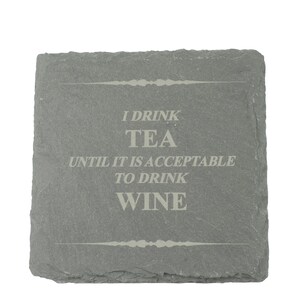 May include: A square, grey slate drinks coaster with the engraved text "I DRINK TEA UNTIL IT IS ACCEPTABLE TO DRINK WINE". The coaster has a rough, textured surface and decorative lines above and below the text.