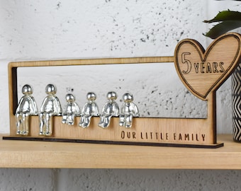 May include: Wooden sign with a heart shape that says "5 Years" and a row of silver figurines sitting on a bench. The sign also says "Our Little Family".