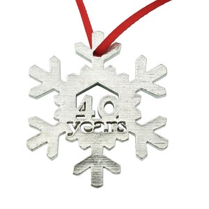Op de afbeelding: Een zilveren sneeuwvlok ornament met een rood lint. De sneeuwvlok heeft "40 jaar" erin gegraveerd.