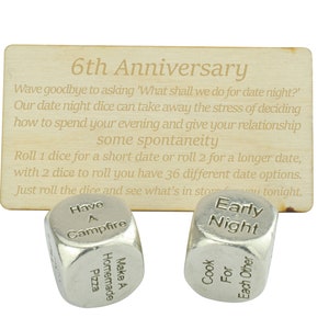 May include: A set of two silver dice with engraved text for a 6th anniversary date night. The dice read "Have a Campfire", "Make a Homemade Pizza", "Early Night", "Cook For Each Other". The dice are on a wooden card with the text "6th Anniversary" and instructions for using the dice.