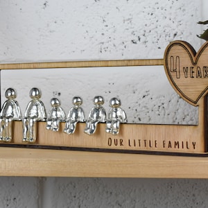 May include: Wooden family figurine display with a heart-shaped plaque that says "4 Years" and the text "Our Little Family". The display features six silver figurines sitting on a wooden ledge.