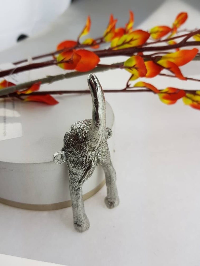 May include: Silver metal dog tail hook. The hook is shaped like a dog's rear end with its tail sticking straight up in the air.