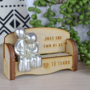 May include: A wooden bench with two silver figurines sitting on it. The bench has the text "Just the two of us" and "17 Years" engraved on it.