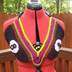 Op de afbeelding: Handgemaakte zwarte gehaakte haltertop met een regenboogafwerking en twee witte achtbalontwerpen. De top wordt getoond op een rode paspop, waarbij de kleurrijke details en het unieke ontwerp worden getoond.