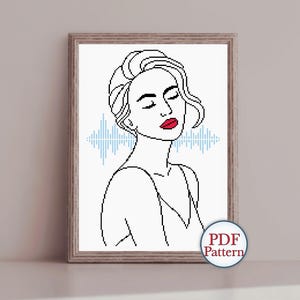 Puede incluir: Una impresión artística enmarcada con un dibujo lineal minimalista de una mujer con los ojos cerrados y labios rojos. La obra de arte incluye un diseño de onda de sonido azul y está etiquetada como "PDF Pattern". El marco es de color marrón claro.
