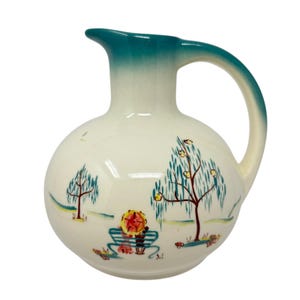 May include: A white ceramic pitcher with a round body and a teal handle and spout. The pitcher features a hand-painted scene of trees, a bench, and flowers. The design is in shades of brown, yellow, and blue.