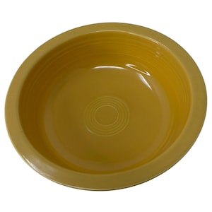May include: A round, deep yellow ceramic bowl with a wide, flat rim. The interior of the bowl features a series of concentric circular ridges embossed into the base, and the overall surface has a smooth, glossy finish with a uniform color.