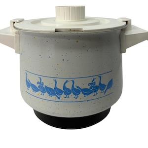 May include: A white speckled pot with a black base and a white lid. The pot features a blue horizontal band decorated with a repeating pattern of blue geese, some wearing bows. It has white side handles and a central knob on the lid.