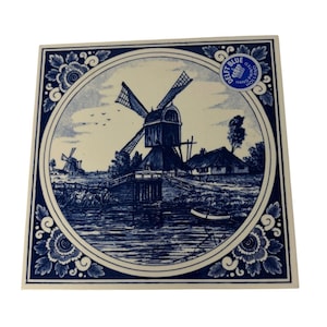 May include: A square ceramic tile featuring a blue and white illustration of a Dutch landscape with a windmill, a small house, and a boat on water. The design is enclosed in a circular border with floral corner accents and a Delft Blue sticker.