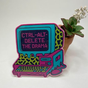 May include: A sticker with a retro computer design and the text "CTRL-ALT-DELETE THE DRAMA." The sticker has a teal screen, a pink and teal body, and a leopard print accent. A small potted succulent is next to the sticker.