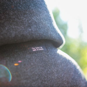May include: A close-up of a gray hooded sweatshirt with a black label that reads "Pink Coder Ltd. MADE IN CANADA".