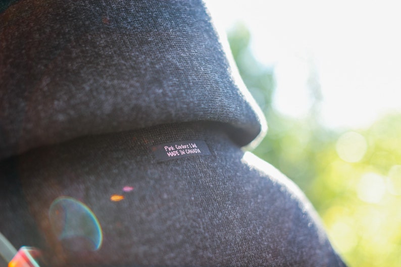 May include: A close-up of a gray hooded sweatshirt with a black label that reads "Pink Coder Ltd. MADE IN CANADA".