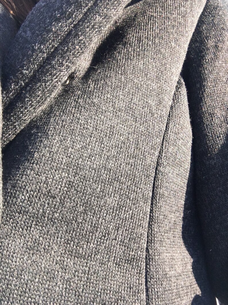 May include: Close-up of a dark gray knitted fabric with a subtle texture. The fabric is soft and appears to be made of a high-quality material.