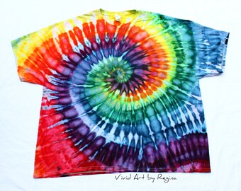 May include: A tie-dye t-shirt with a rainbow spiral design. The shirt is a light blue color with shades of yellow, orange, red, green, blue, and purple. The design is centered on the shirt and is surrounded by a white border. The shirt has a crew neck and short sleeves. The text "Vivid Art by Regina" is printed on the bottom of the shirt.