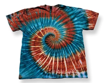 May include: A tie-dye t-shirt with a spiral pattern in shades of blue, orange, and red. The shirt has a white background and the text "Vivid Art by Regina" is printed on the bottom.