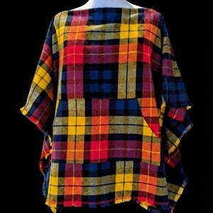 May include: A colorful plaid poncho in shades of red, yellow, blue, and orange. The poncho has a square neckline and a fringed hem. The fabric appears to be a woven material, possibly wool or a wool blend.
